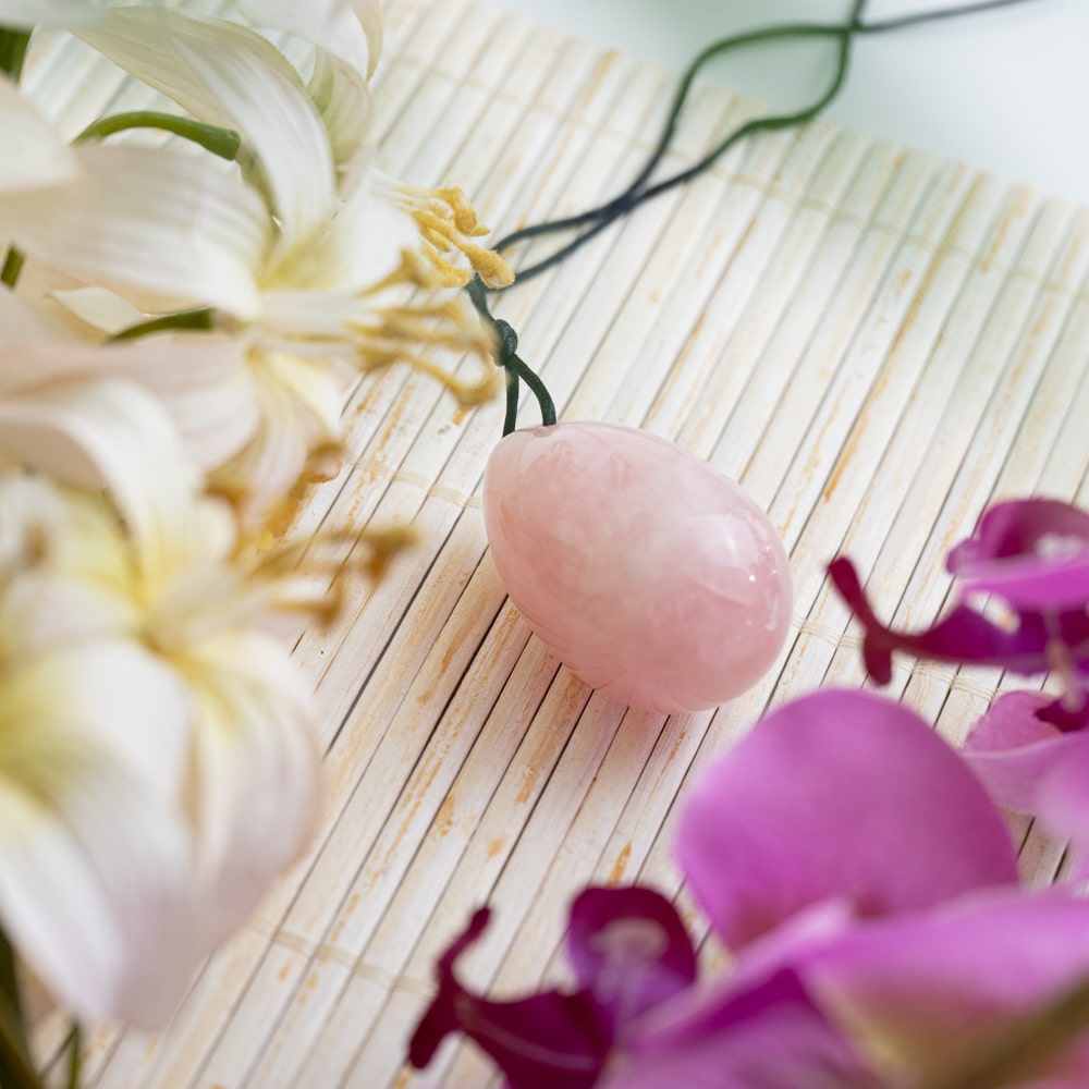 rose quartz yoni egg on bamboo mat with flowers
