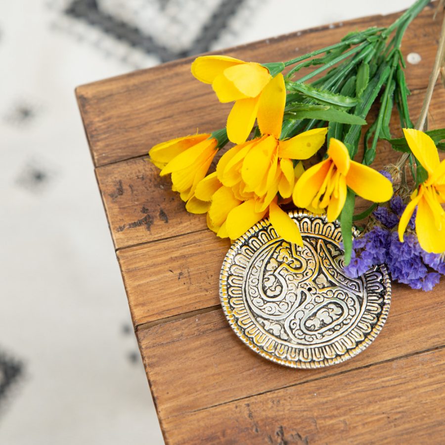 round gold colored ohm incense holder with yellow flowers on table