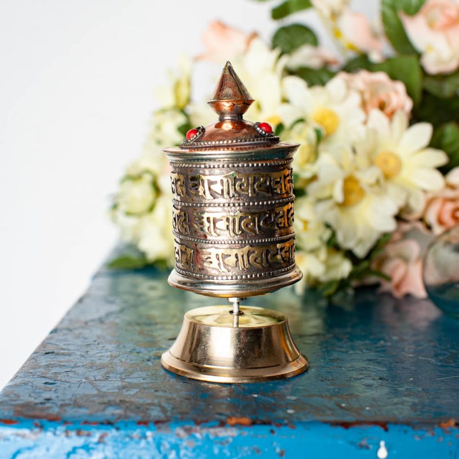 brass tibetan prayer wheel with pink and white flowers on blue chest