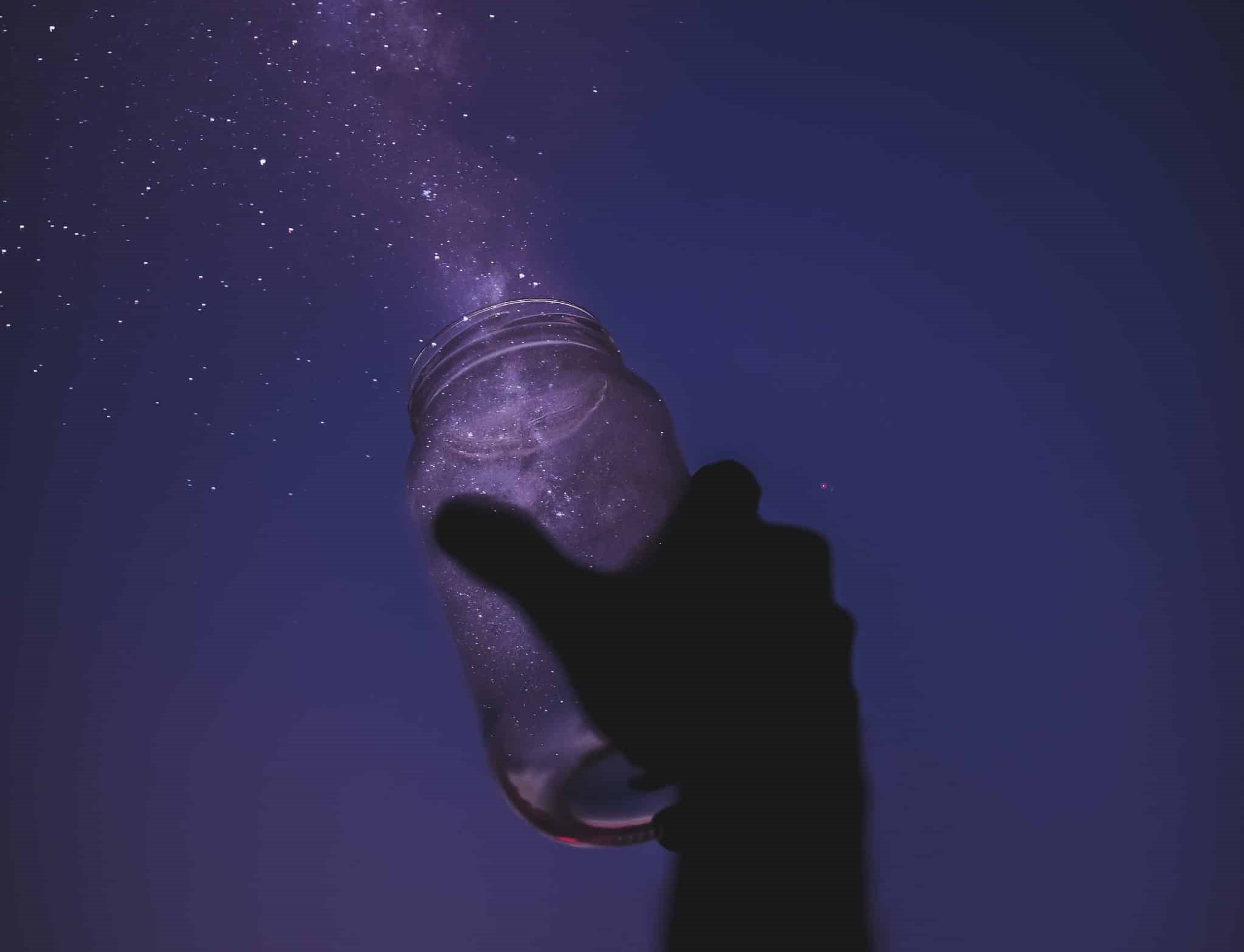 hand silhouette capturing stars in mason jar