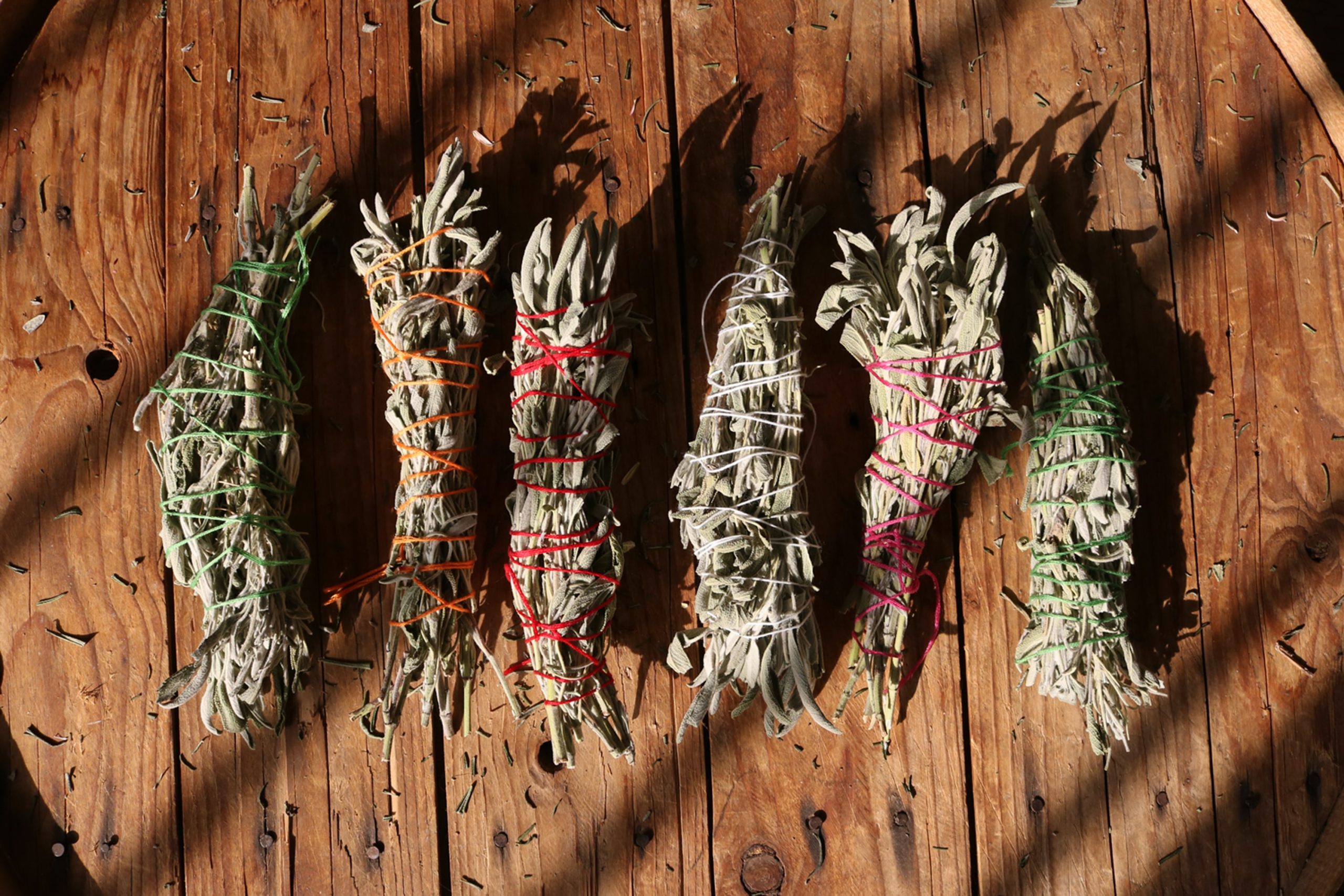 dried homemade white sage smudge sticks in sunlight on wooden table