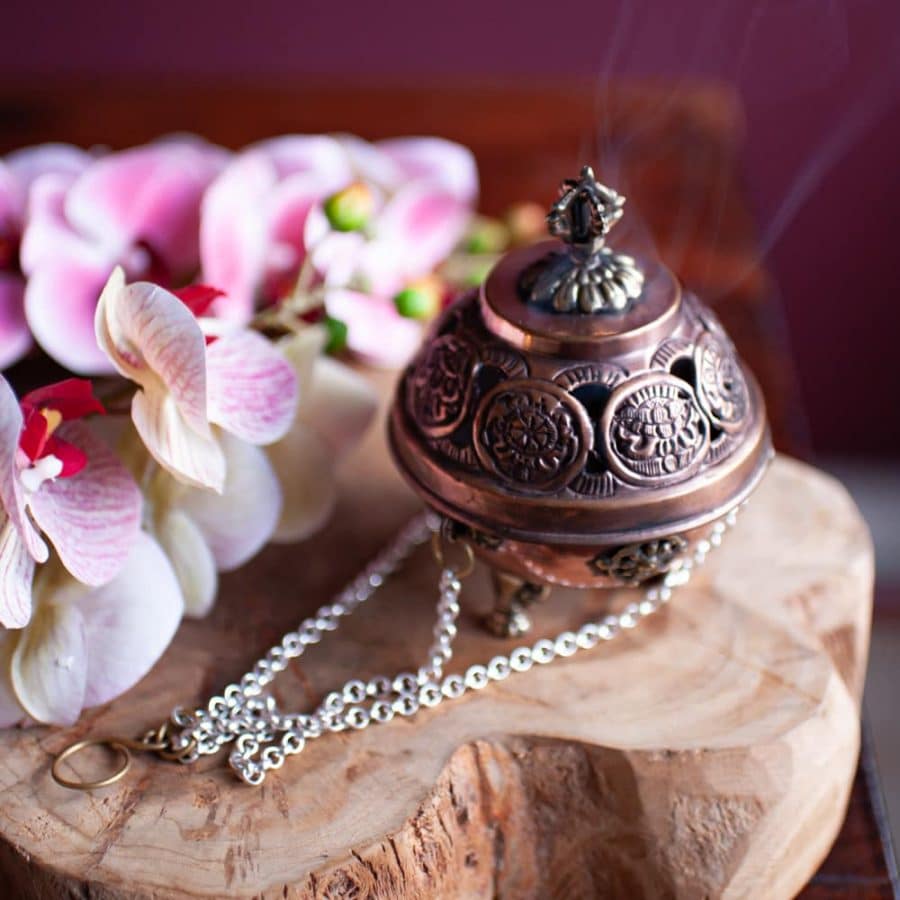 hanging brass incense burner on wood with orchids